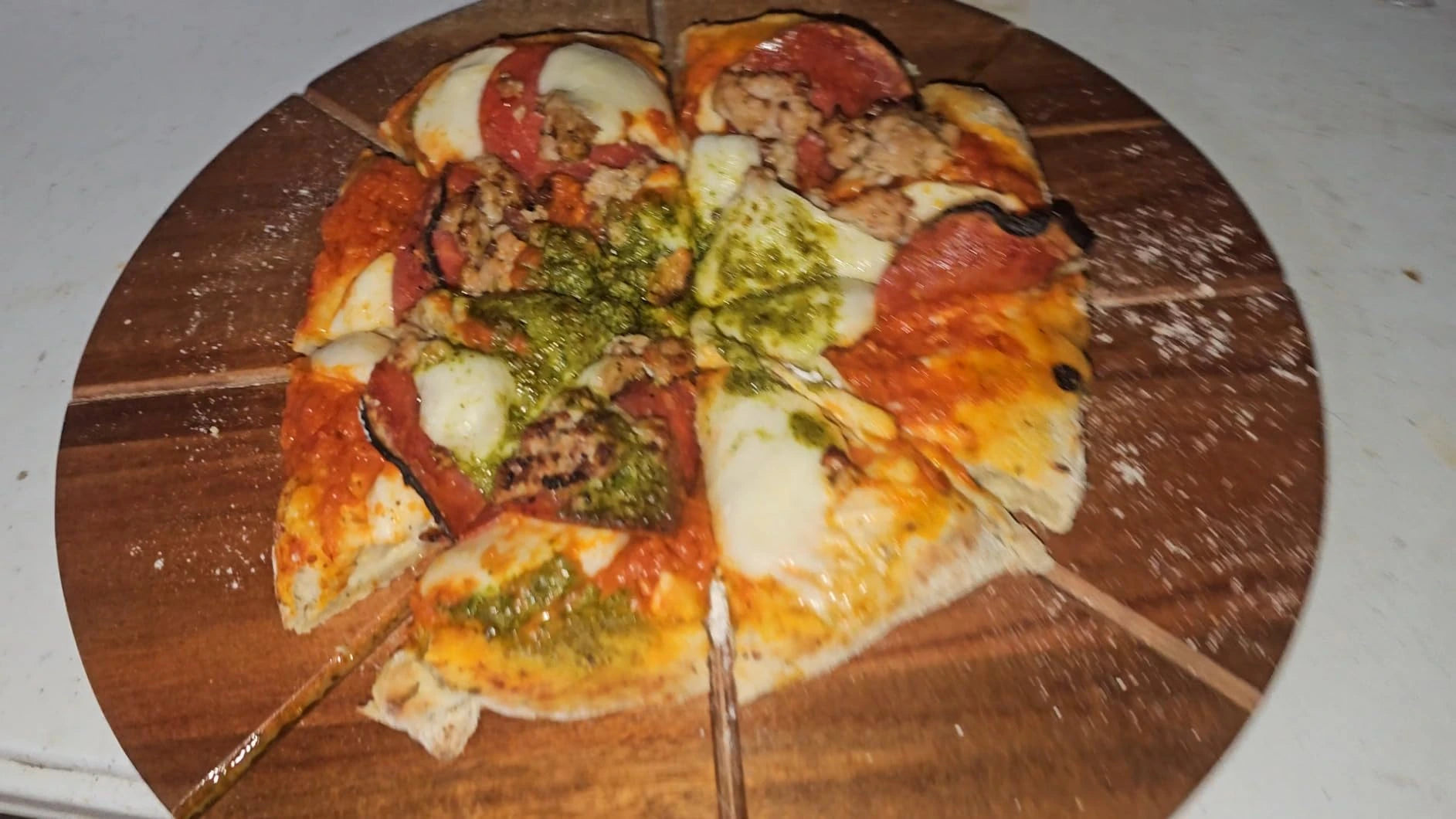 A freshly baked pepperoni and pesto pizza sliced on a round wooden board