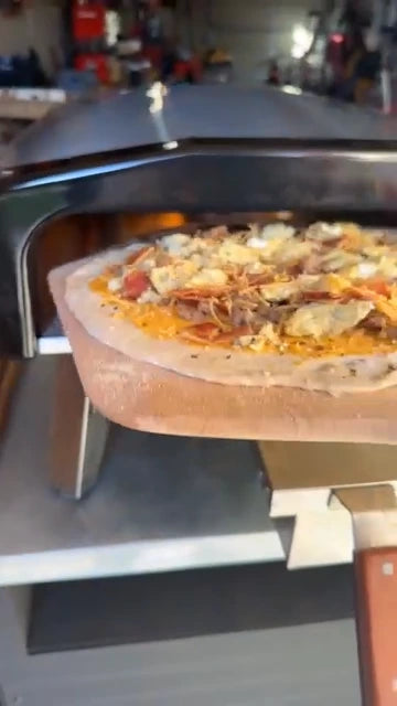A pizza being inserted into the oven using a wooden pizza peel